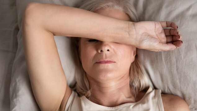 Plan rapproché du visage d'une femme couchée sur un lit, l'avant-bras posé sur le front.