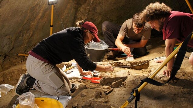 Trois archéologues fouillent le sol d'une grotte.