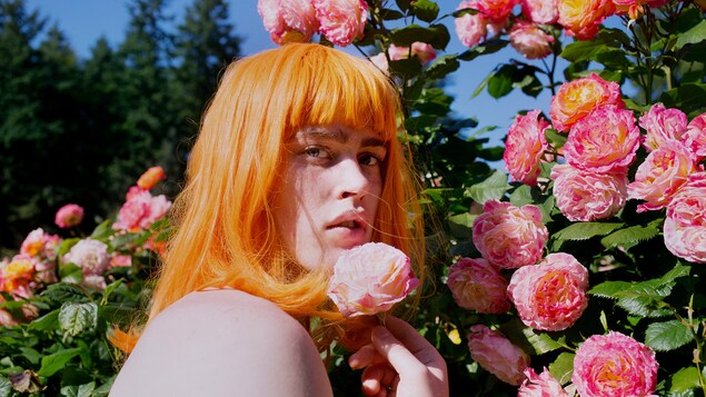 Portrait très coloré où l'on voit un homme à la perruque orange près d'un bosquet rempli de fleurs.