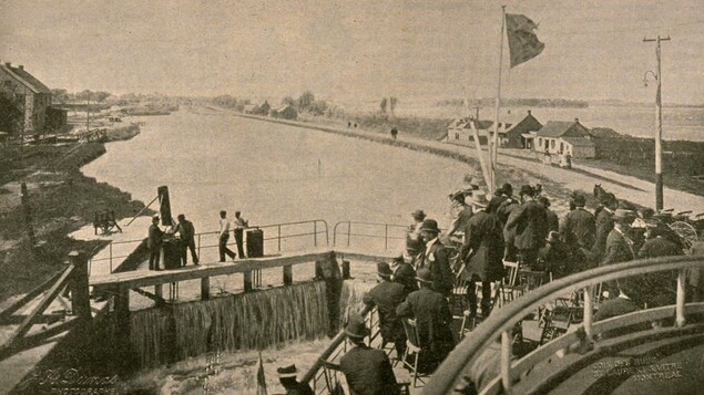 Image d'époque montrant des personnes sur le pont d'un bateau voguant sur un canal.