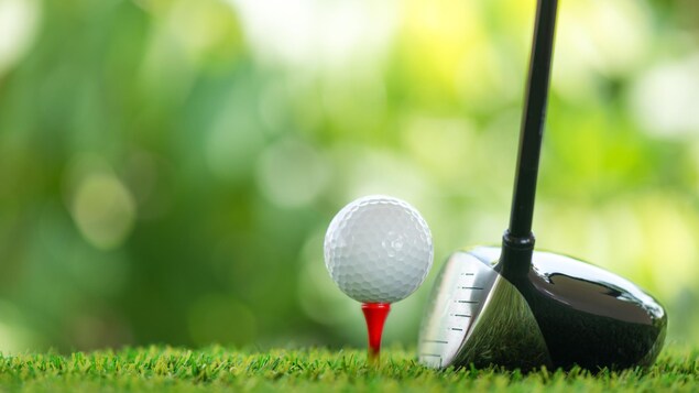 Une balle de golf sur un tee, avec un bâton à côté.