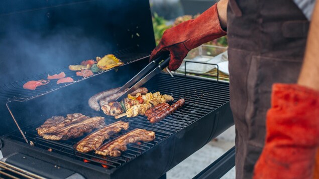 Un homme fait cuire des saucisses, de la viande et des brochettes sur le barbecue.
