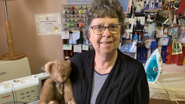 Une femme souriante, portant des lunettes, tient un ourson en fourrure dans ses bras
