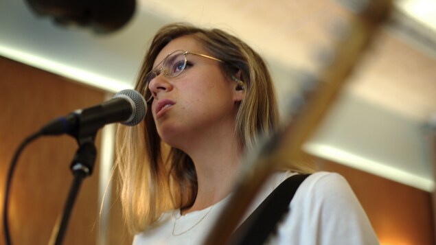 Lydia Képinski chante derrière un micro, une guitare à la main.