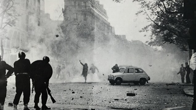 Photo en noir et blanc montrant des policiers face à des citoyens qui leur lance des pavés dans une rue de Paris.