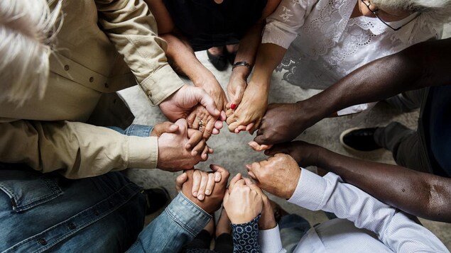 Sept personnes d'origines ethniques différentes se tiennent les mains ensemble en un cercle.