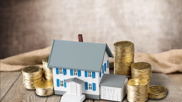 Une maison miniature est entourée de pièces de monnaie.