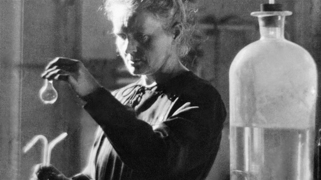 Marie Curie tient une fiole dans ses mains. 
