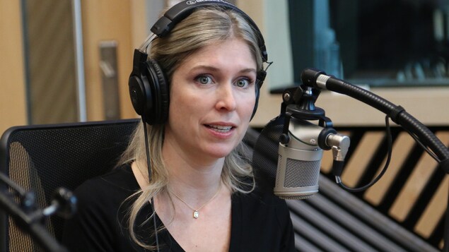 Une femme, casque d'écoute sur la tête, parle dans un micro dans un studio de radio. 