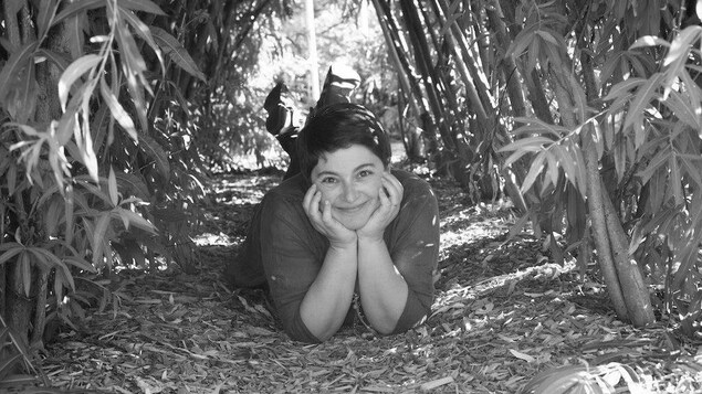 Marie Lacrampe sourit, couchée au sol sous une arche de bambou.