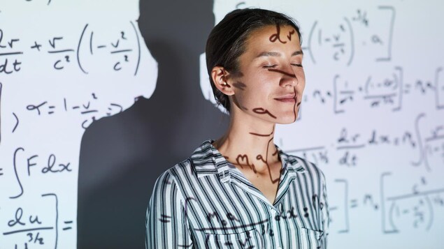 Une femme, les yeux fermés, contre un tableau blanc sur lequel sont projetées des formules mathématiques. 