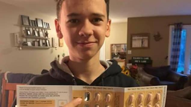 Un adolescent sourit en tenant dans sa main une boîte de médicaments.