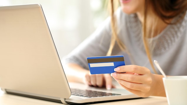Une jeune femme effectue un achat en ligne avec son ordinateur portable et sa carte de crédit.