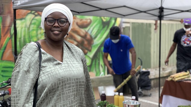 Khadyja Ndoye pose devant une murale pendant qu'une personne coupe de la canne à sucre.
