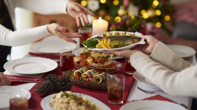 Des gens passent une assiette de poisson à une table bien garnie pour les Fêtes.