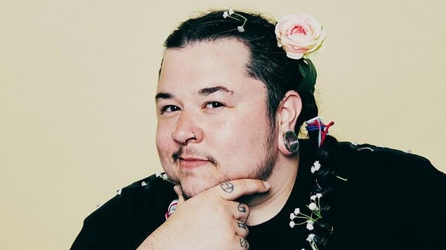 L'artiste pose avec une main sur le menton; il porte une rose dans ses cheveux