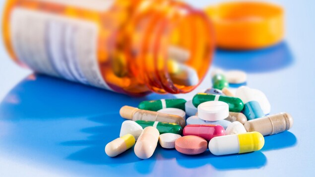 Des pilules de différentes couleurs à côté d'une bouteille de médicaments renversée.