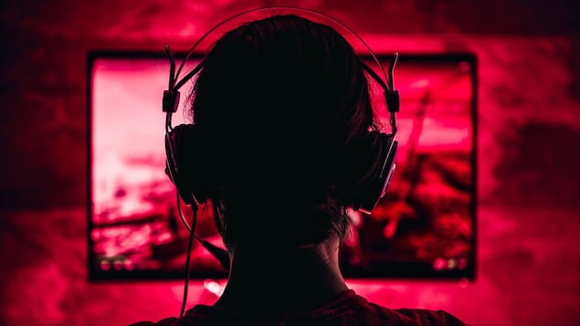 Une personne, de dos, joue à un jeu vidéo dans un éclairage rouge.