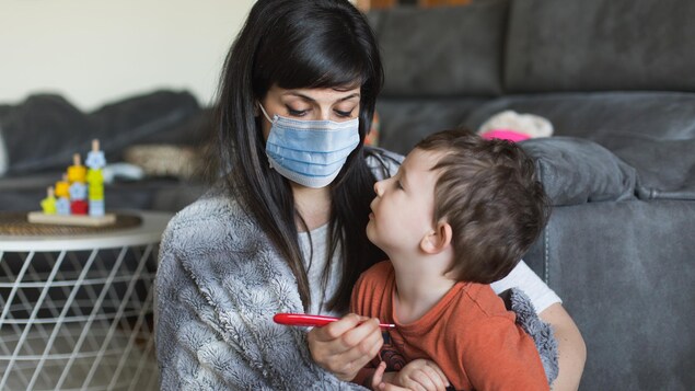 Une mère porte un masque et prend la température de son fils.