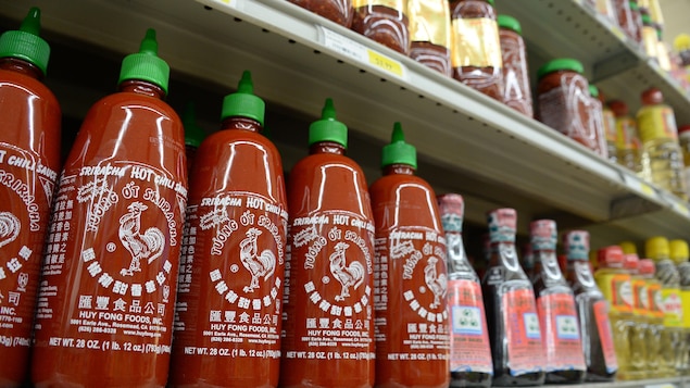 Des bouteilles de sauce sriracha sont alignées dans le présentoir d'une épicerie.