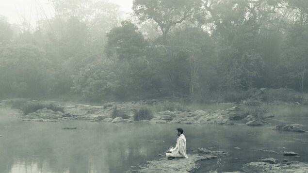 Un homme médite sur le rocher d'une rivière.