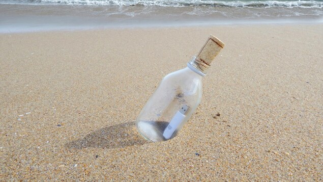 Une clé USB dans une bouteille en verre sur une plage.
