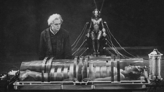 Scène du film Metropolis de Fritz Lang illustrant un homme devant le corps allongé d'une personne dans un grand tube de verre