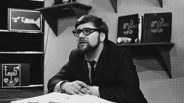 Dans un studio de télévision, l'animateur Michel Garneau, assis à son bureau.