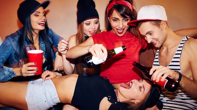 Quatre jeunes femmes et un jeune homme s'adonnent à un jeu avec de l'alcool.