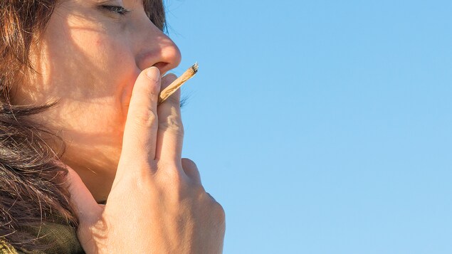Une femme vue de profil fume un joint sous un ciel bleu.