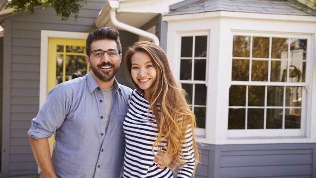 Un homme de race blanche et une femme asiatique se tiennent devant une maison.