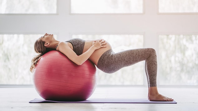 Une femme enceinte fait des exercices avec un ballon thérapeutique.