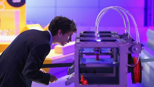 Un homme regarde une imprimante 3D à l’œuvre.