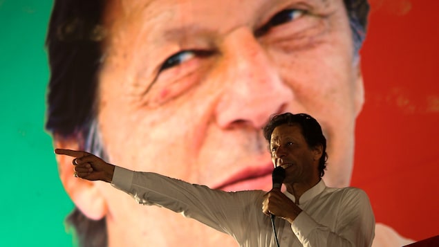 Imran Khan parle au micro devant une image géante de lui en arrière-plan.