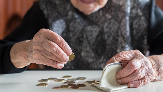 Un dame âgée conte ses sous, posés sur une table devant elle.