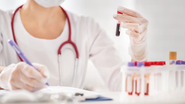 Une travailleuse médicale analyse un échantillon de sang contenu dans une éprouvette.