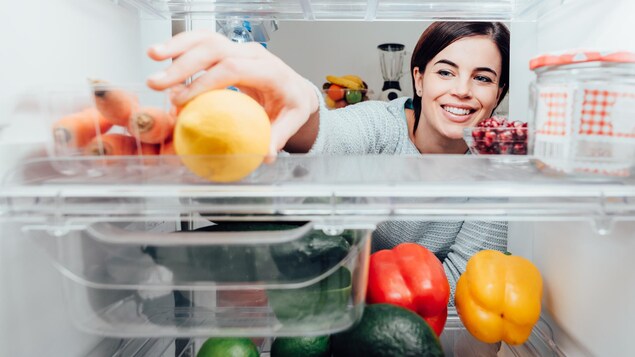 Une femme saisit un citron dans un réfrigérateur ouvert.