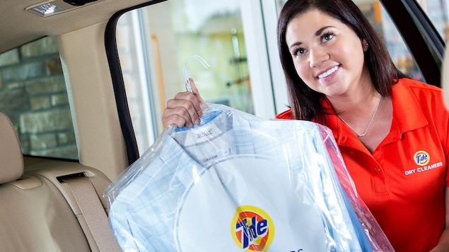 Une employée du service Tide Dry Cleaners tient des vêtements dans l'embrasure d'une portière de voiture.