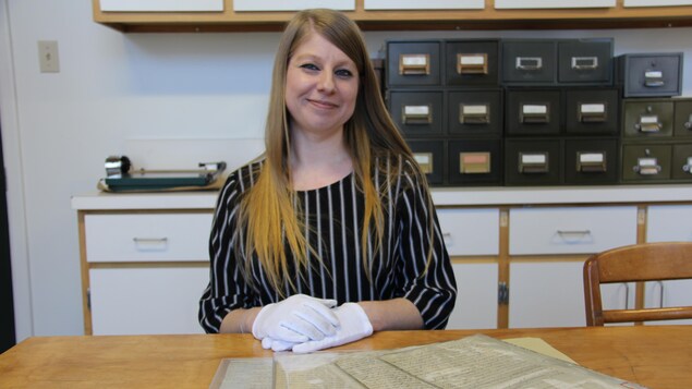 Une femme prend la pose avec des gants blancs déposés sur des documents d'archives.
