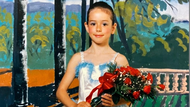 Une jeune fille en tenue de danse claissique tenant un bouquet de rose dans ses bras.