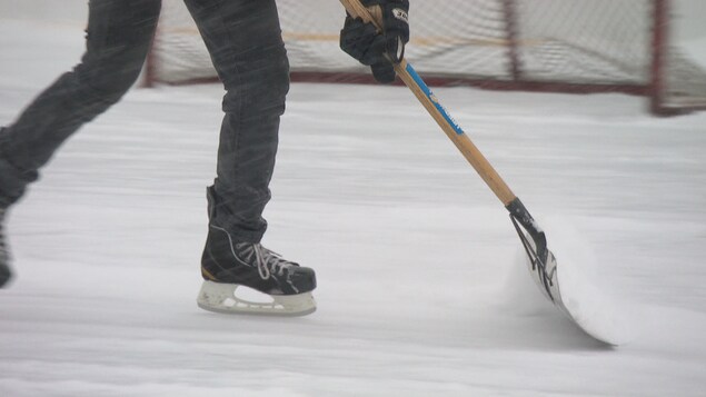Un homme pousse une pelle pour déblayer sur une patinoire extérieure de hockey.