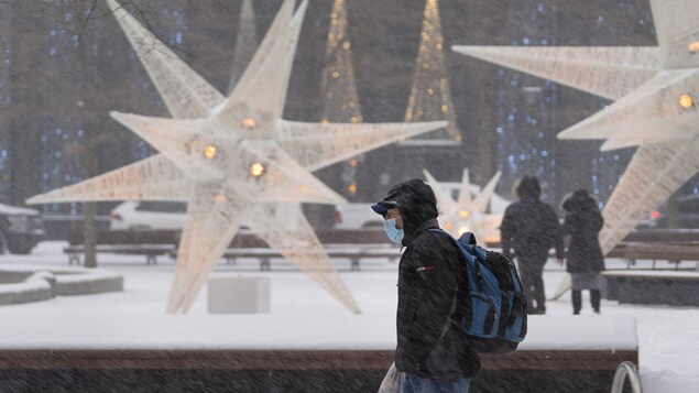 Des passants marchent dans un parc où l'on voit de grandes étoiles blanches pendant que la neige tombe fortement.
