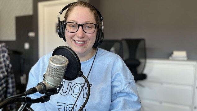 Lindsey Chamberlain est assis devant un micro du studio 1 de la station de Radio-Canada sur la rue Elm à Sudbury. Elle regarde l'objectif de la caméra en souriant.