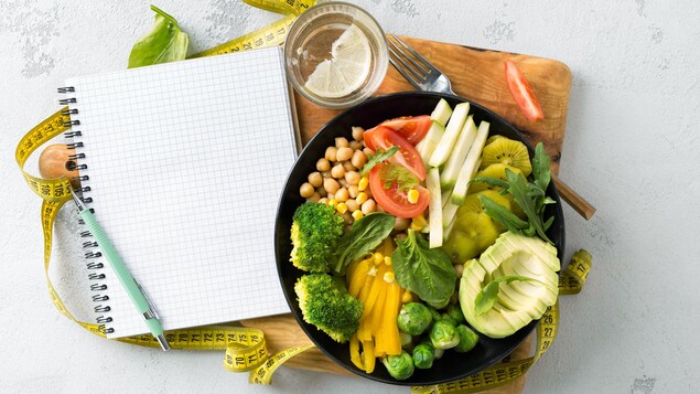 Une assiette remplie de légumes, avec un calepin de notes et un ruban à mesurer.