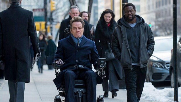 Bryan Cranston est en triporteur sur le trottoir. Kevin Hart marche à ses côtés.  