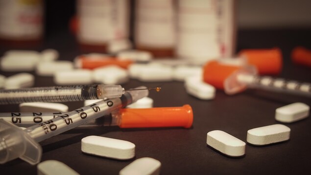 Une seringue usagée et des médicaments d'ordonnance sont éparpillés de façon désordonnée.
