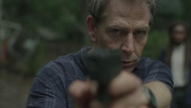 Un homme blanc dans la cinquantaine pointe un revolver dans notre direction.