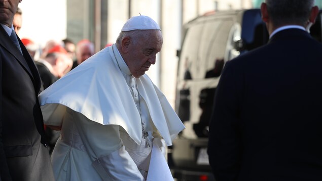 Portrait du pape François, l'air pensif, entouré d'homme en costumes.