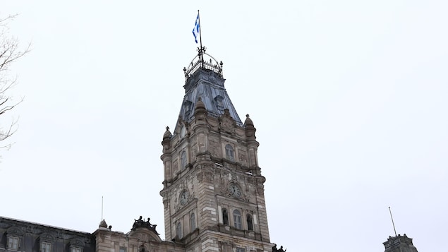 Gros plan sur la tour centrale de l'édifice sur laquelle le drapeau du Québec flotte sur un mât.