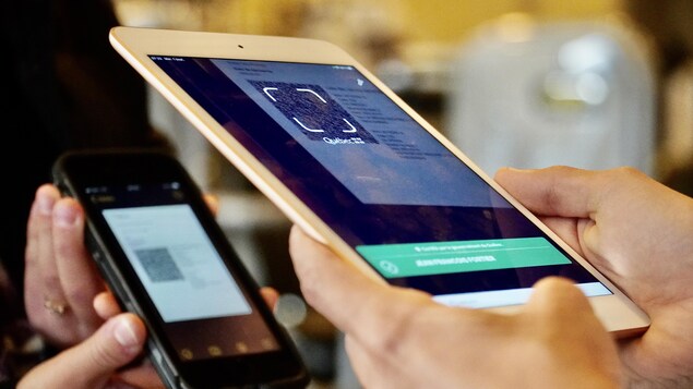 Une employée tient une tablette électronique pour lire un code QR sur le téléphone d'une cliente.